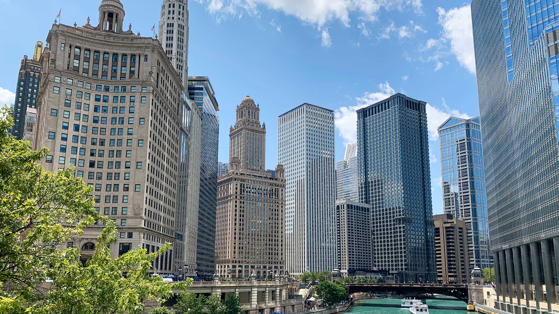 A Chicago cityscape along the Chicago river in summer. The sky is blue with a few clouds.